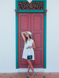 Woman in a white dress standing in front of a red door with teal trim