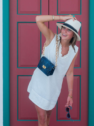 Woman in a white dress and hat posing in front of a red door.