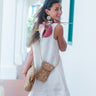 Woman in a white dress with a bambi print bag and gold clutch walking outdoors.