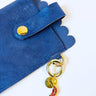 Blue suede glasses clutch with gold accents and a keychain on a white background